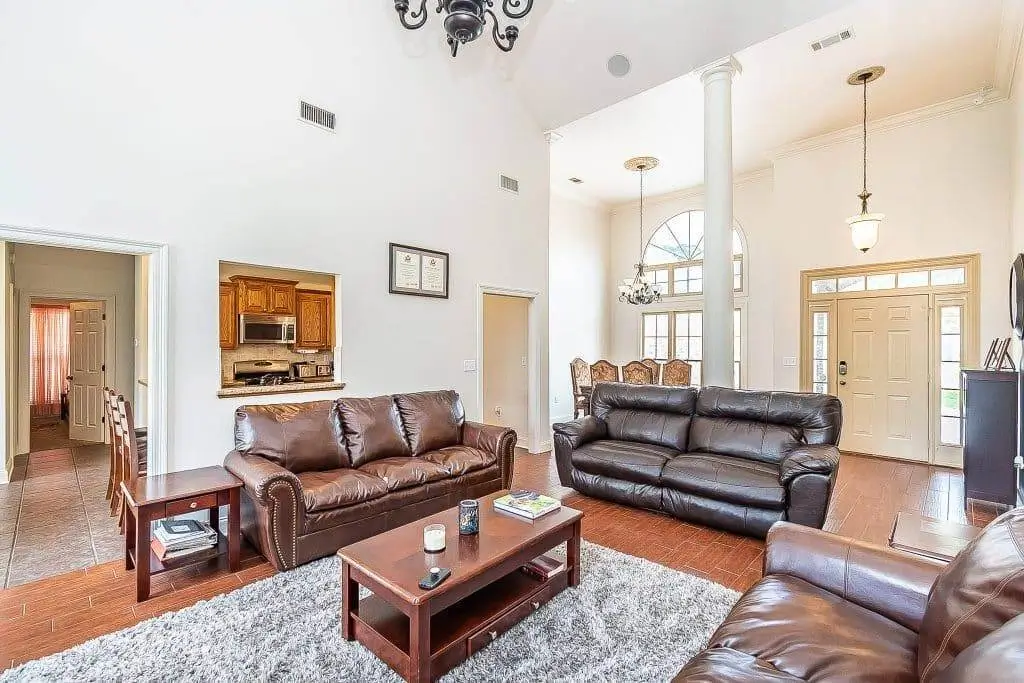 A spacious, high-ceilinged living room with leather sofas, hardwood floors, and elegant lighting fixtures.
