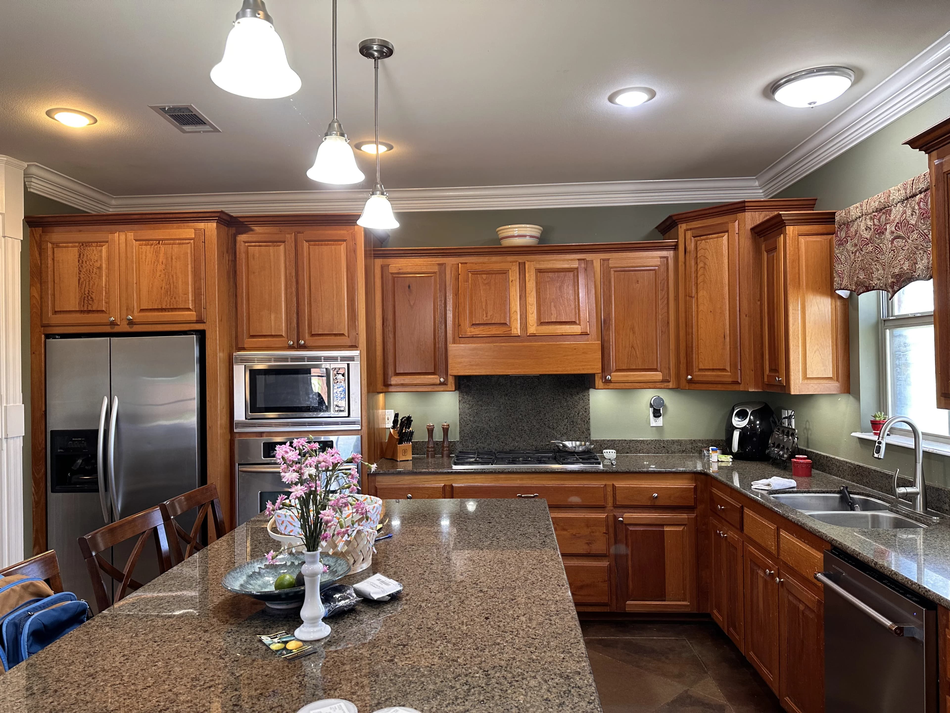 A cozy kitchen with rich wooden cabinets, granite countertops, and stainless steel appliances under warm pendant lighting.
