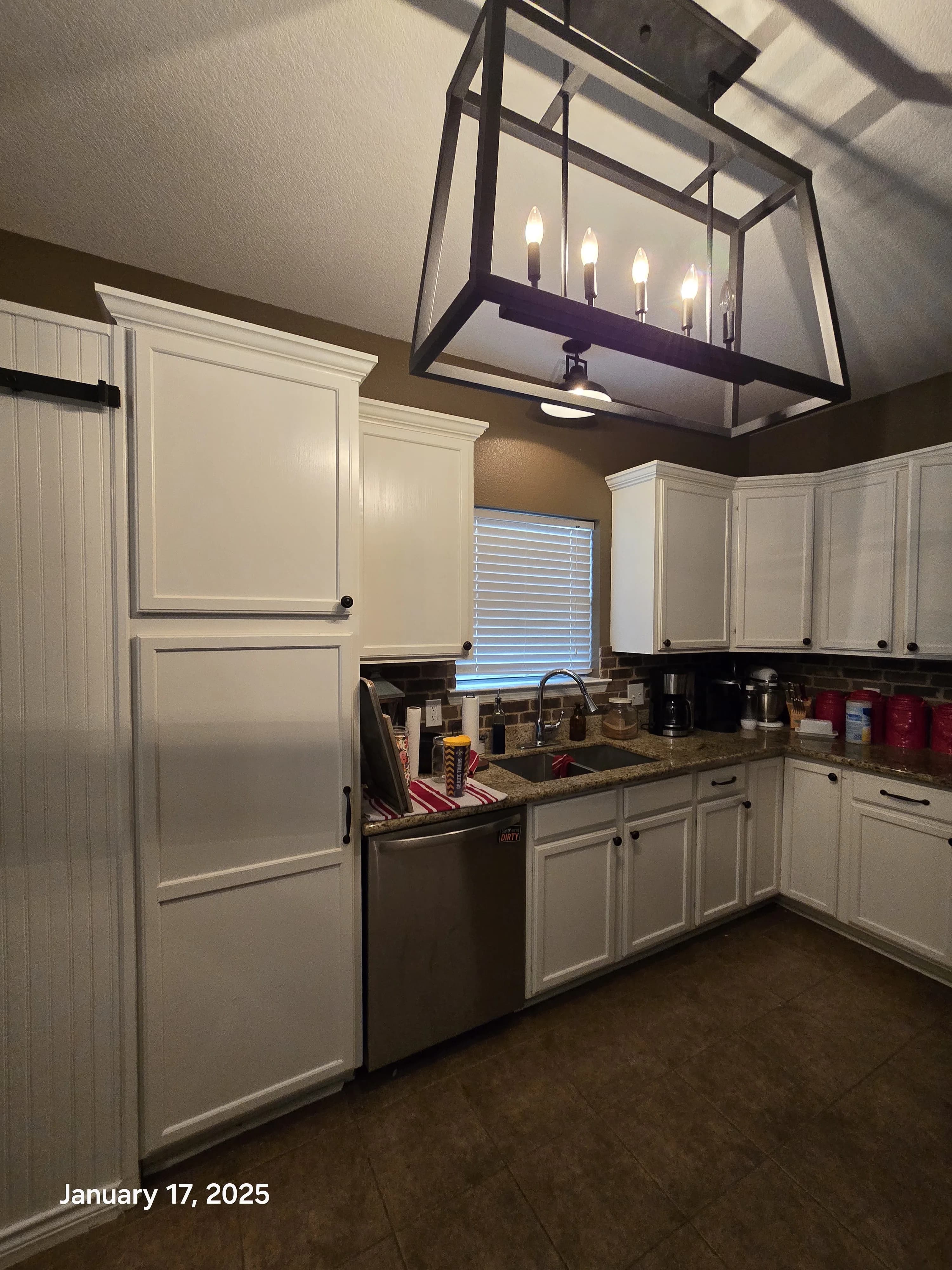 A well-lit kitchen featuring white cabinets, a stainless steel sink, and a large geometric pendant light hanging above the counter.